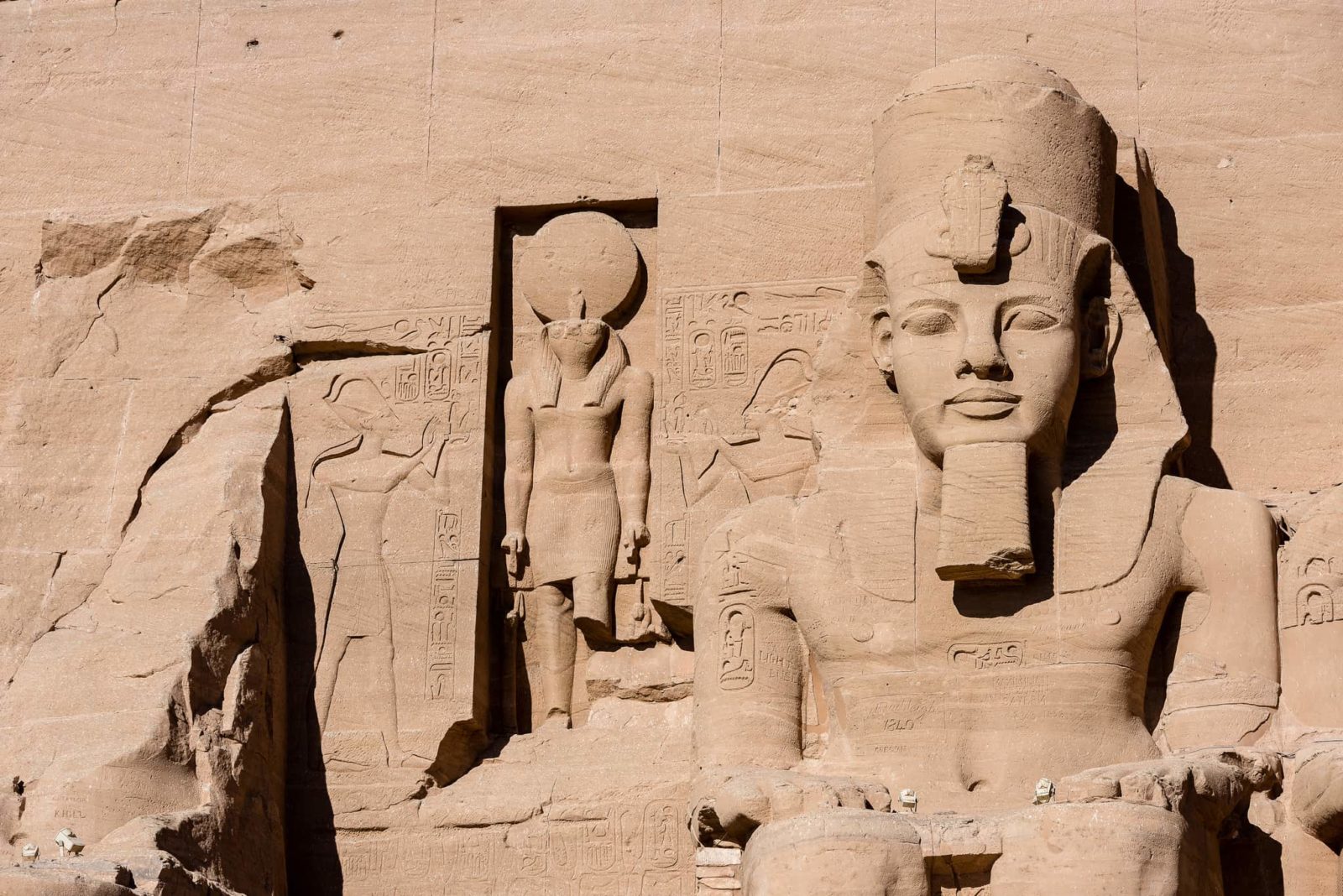 Ancient Egypt stone statues with intricate carvings on a weathered surface.