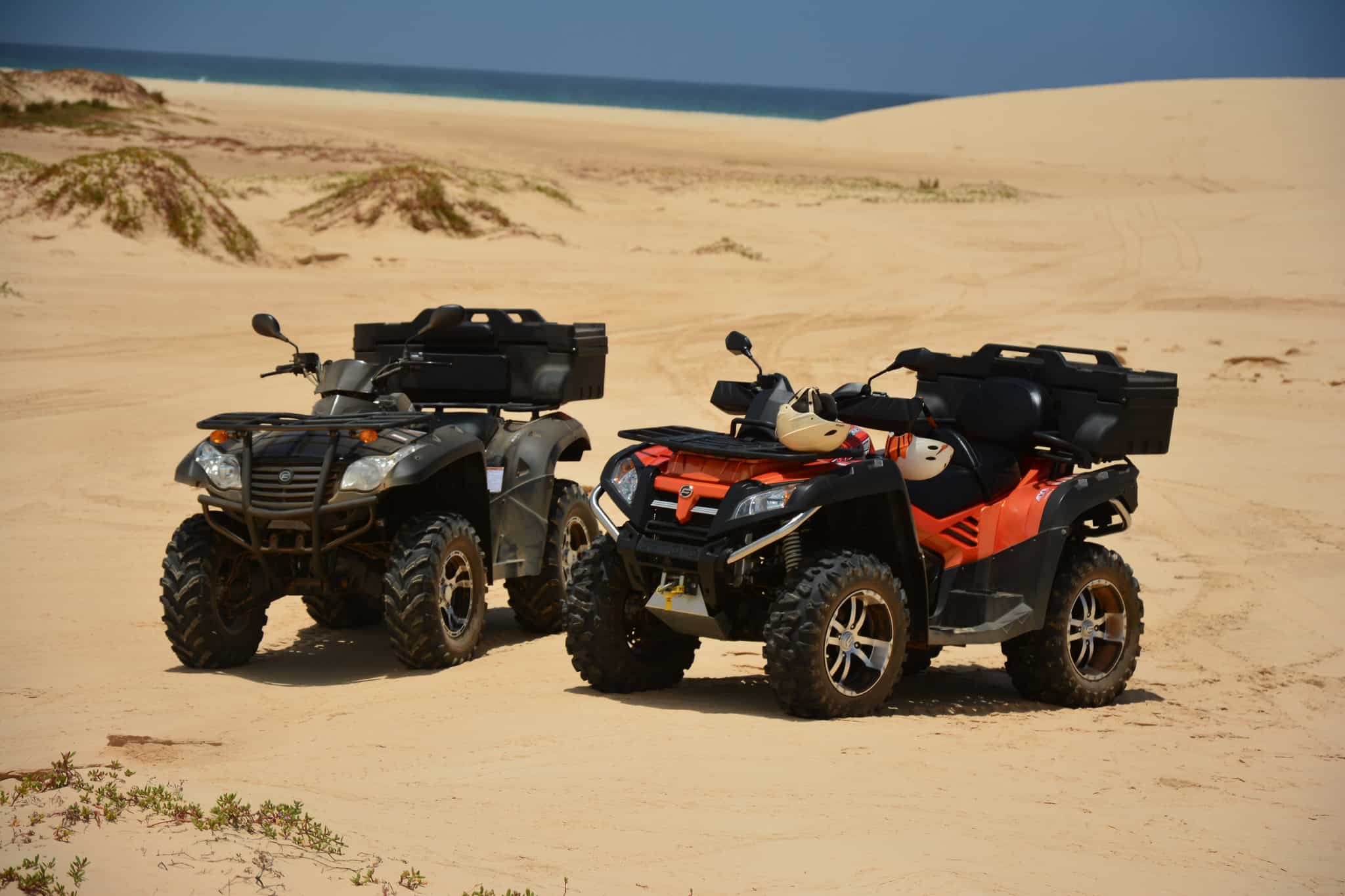 Two all-terrain vehicles rest on a sandy beach by the Red Sea under a clear blue sky.