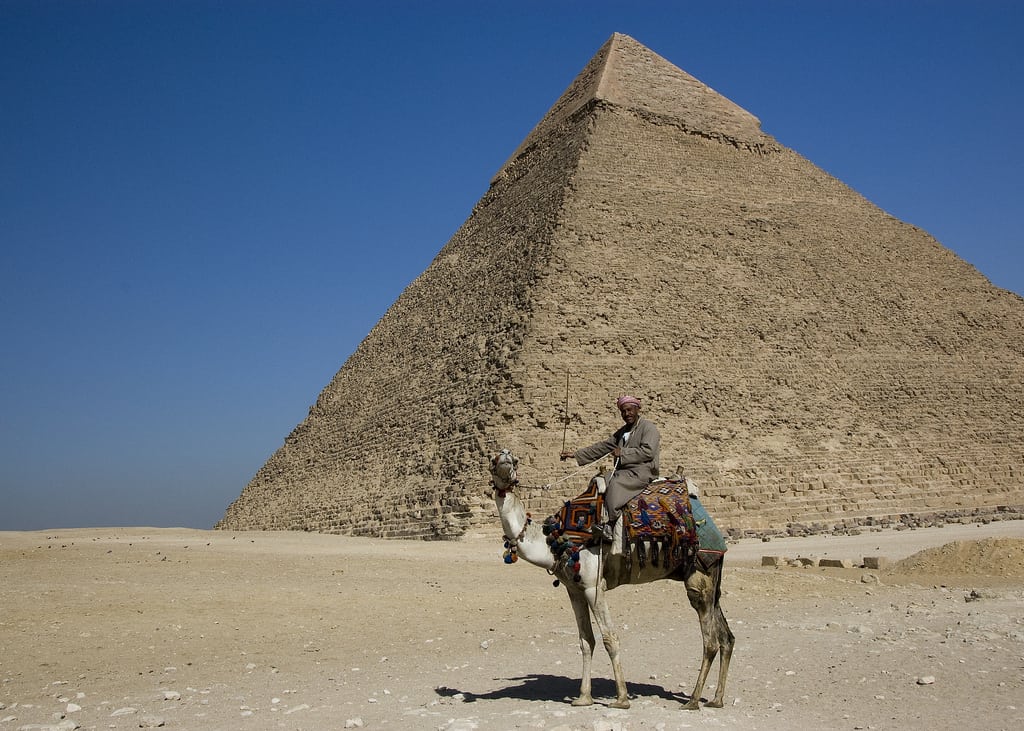 Riding a camel by the pyramid, an essential Egyptian adventure under a clear blue sky.