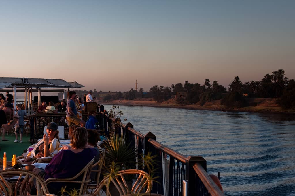 People relaxing on a boat deck at sunset, overlooking wildlife on the Niles calm waters.