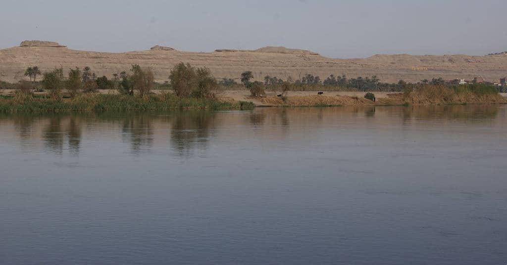 Tranquil Nile with distant hills and sparse vegetation under a clear sky.