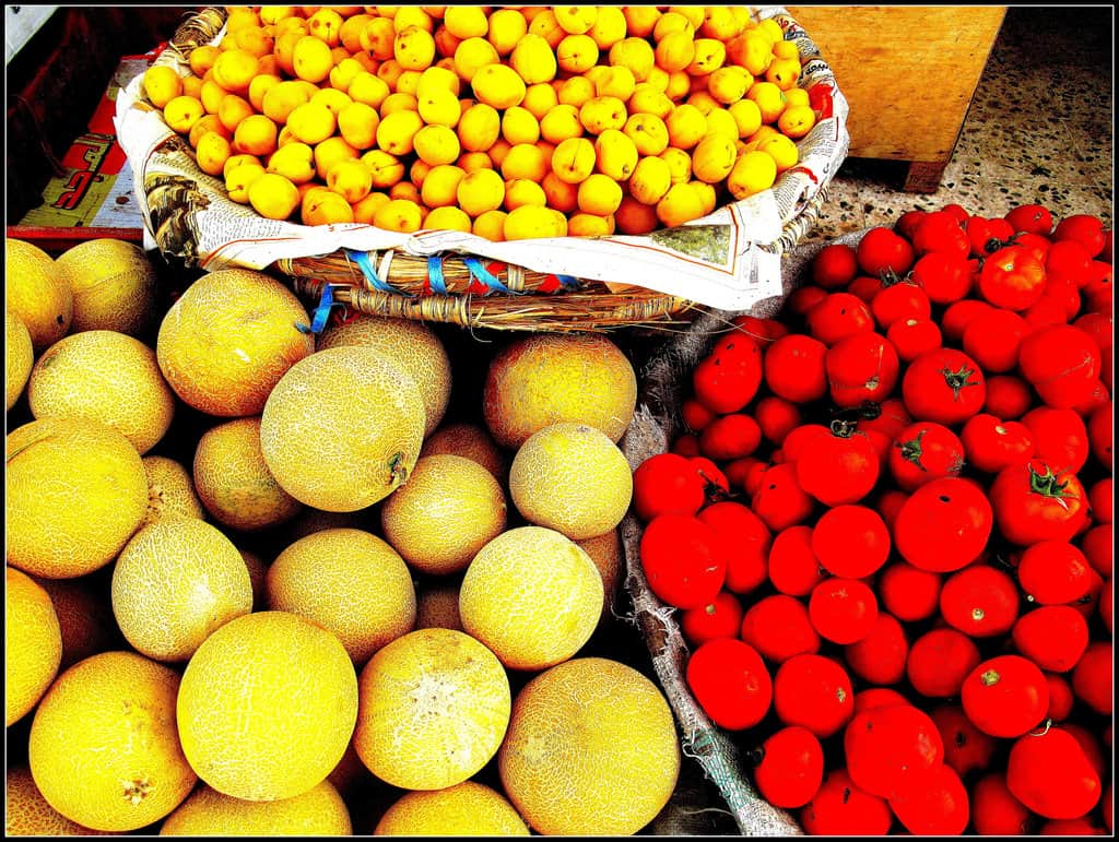 Market stalls in Luxor with baskets of apricots, melons, and tomatoes on display.