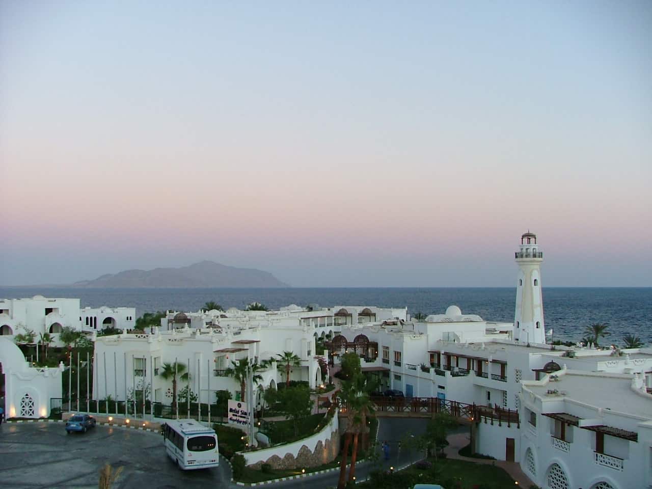 Sharm El Sheikh resort with white buildings, a lighthouse, and a distant island at sunset.