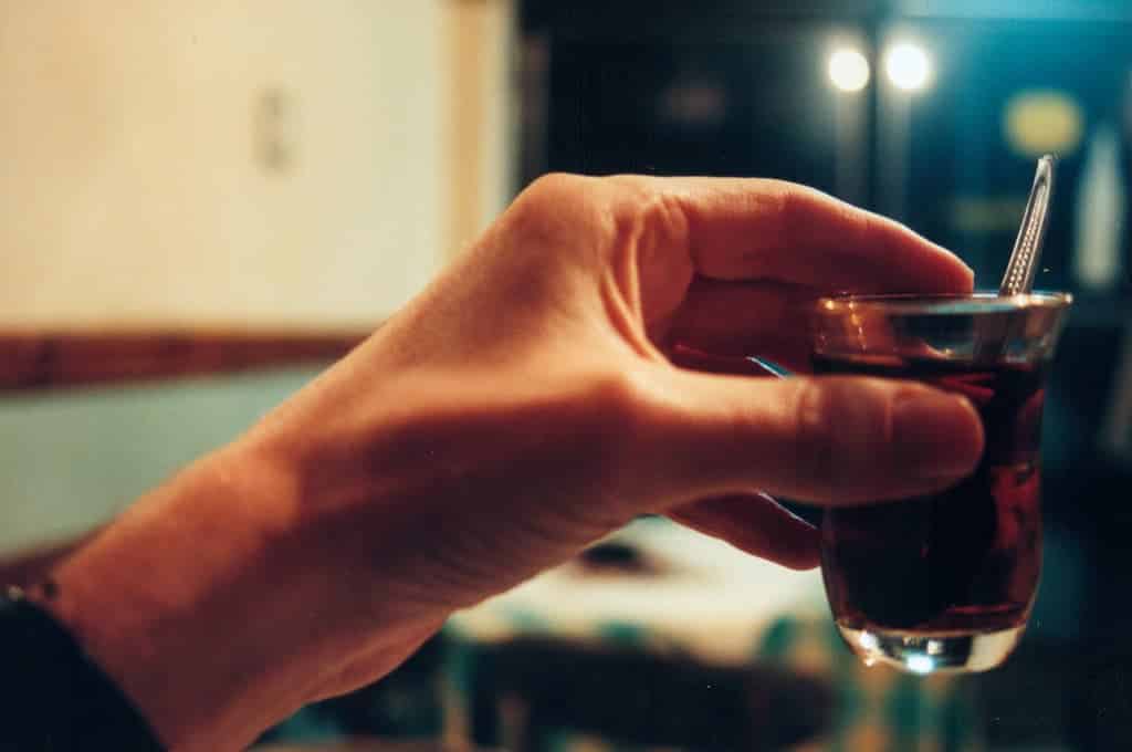 Top 5 drinks to try: Hand holding a small glass of tea with a spoon inside.