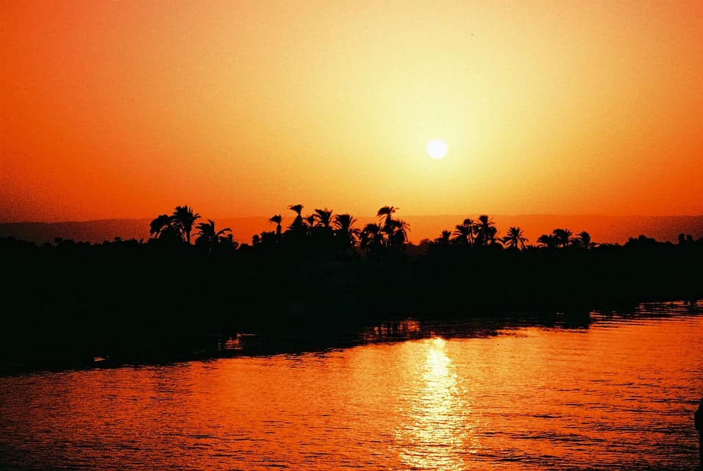 Sunset over a river on a Nile cruise, silhouetted trees against an orange sky.