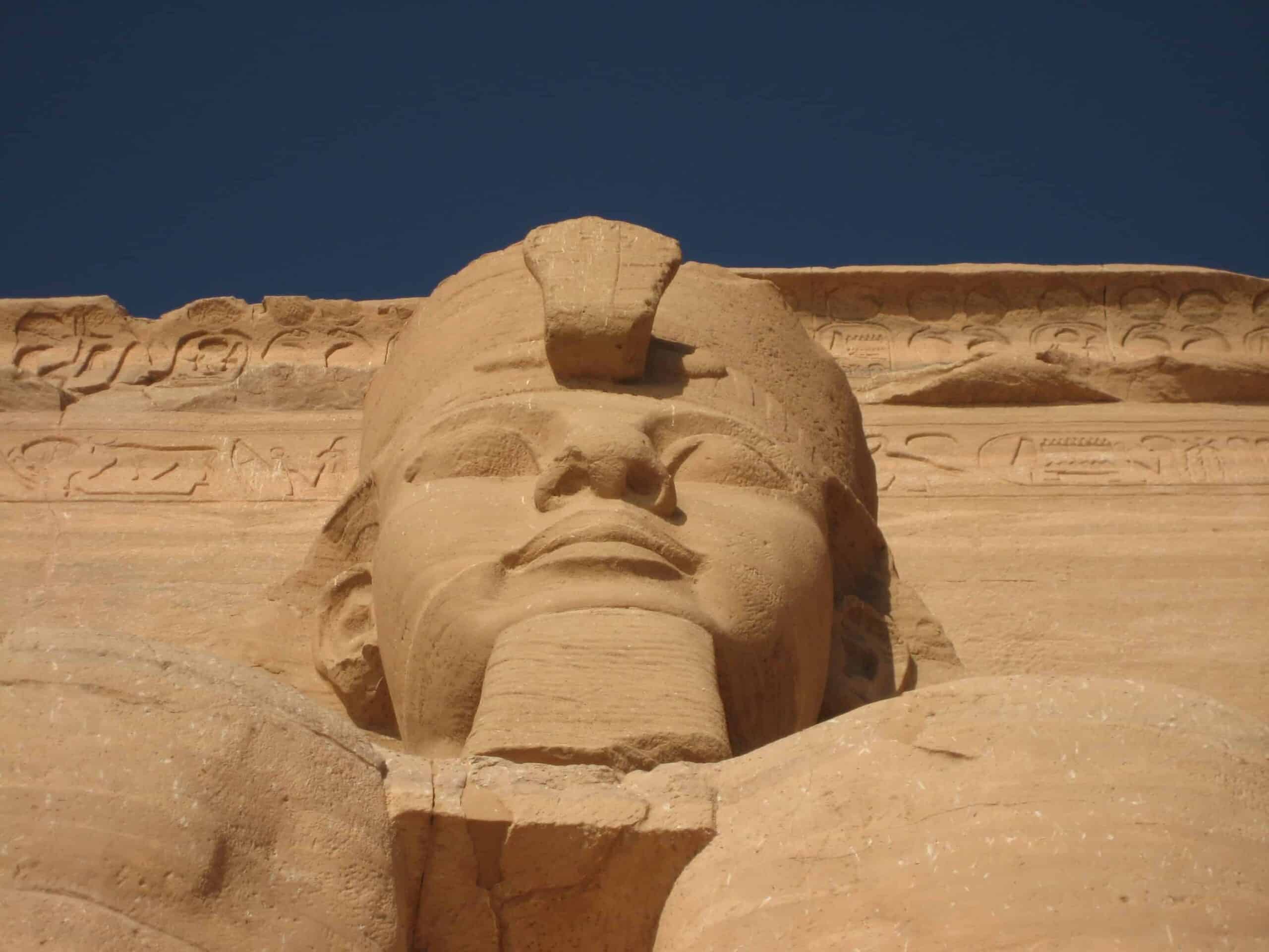 Ancient Egyptian statues face under blue sky, more than just pyramids.