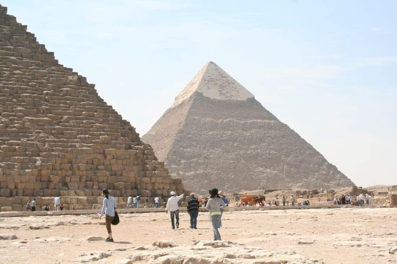 People walk near the Giza Pyramid in a desert landscape under a clear sky.