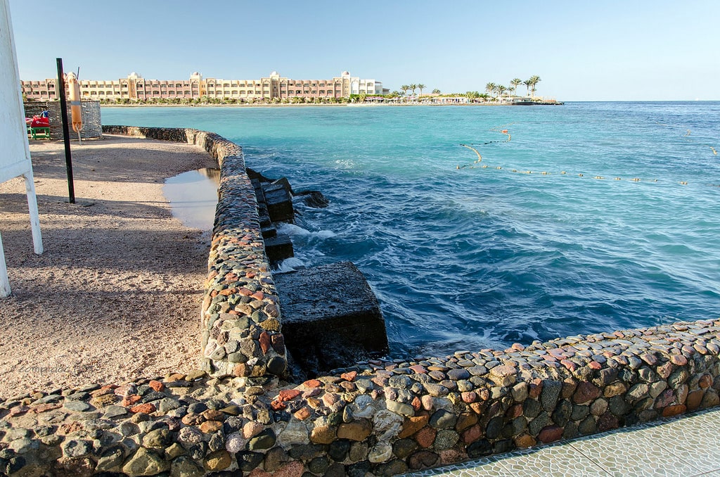 Stone walkway by the ocean with a distant hotel, palm trees, and thoughts of a winter Nile cruise.