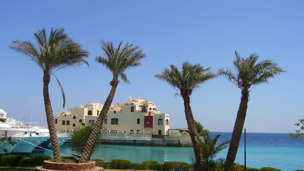 Palm trees and a building by the blue sea in Hurghada, Egypt, under a clear sky.