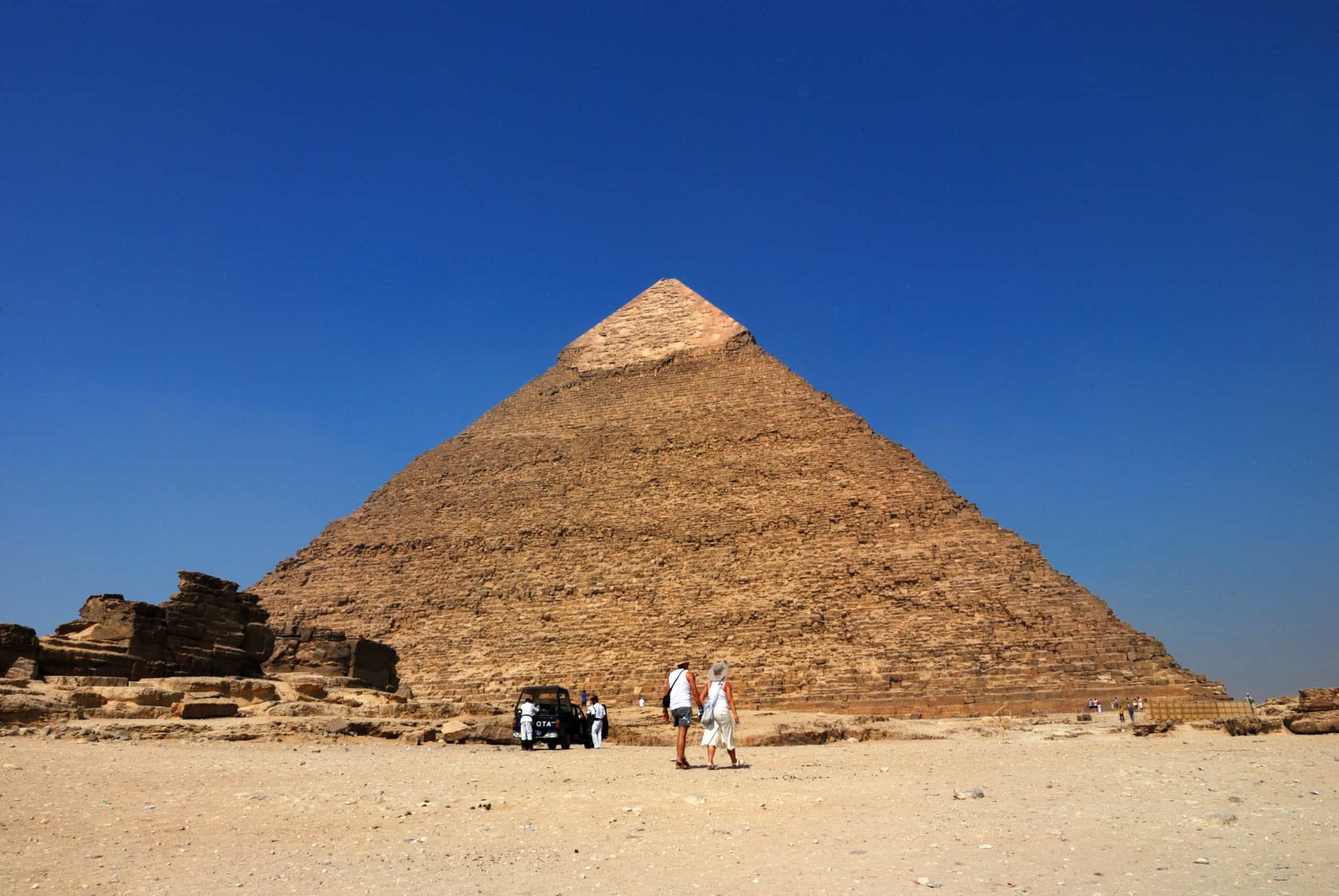 Two people wander by the Great Pyramid, a scene fit for an Egypt film, under a clear blue sky.