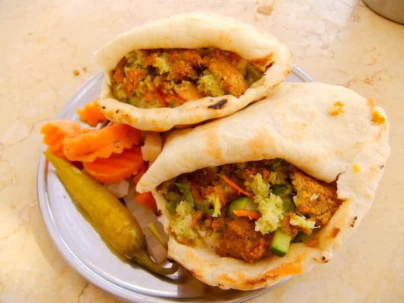 Two pita breads stuffed with falafel, veggies, a must-try in Egypt on a metal plate with pickled sides.