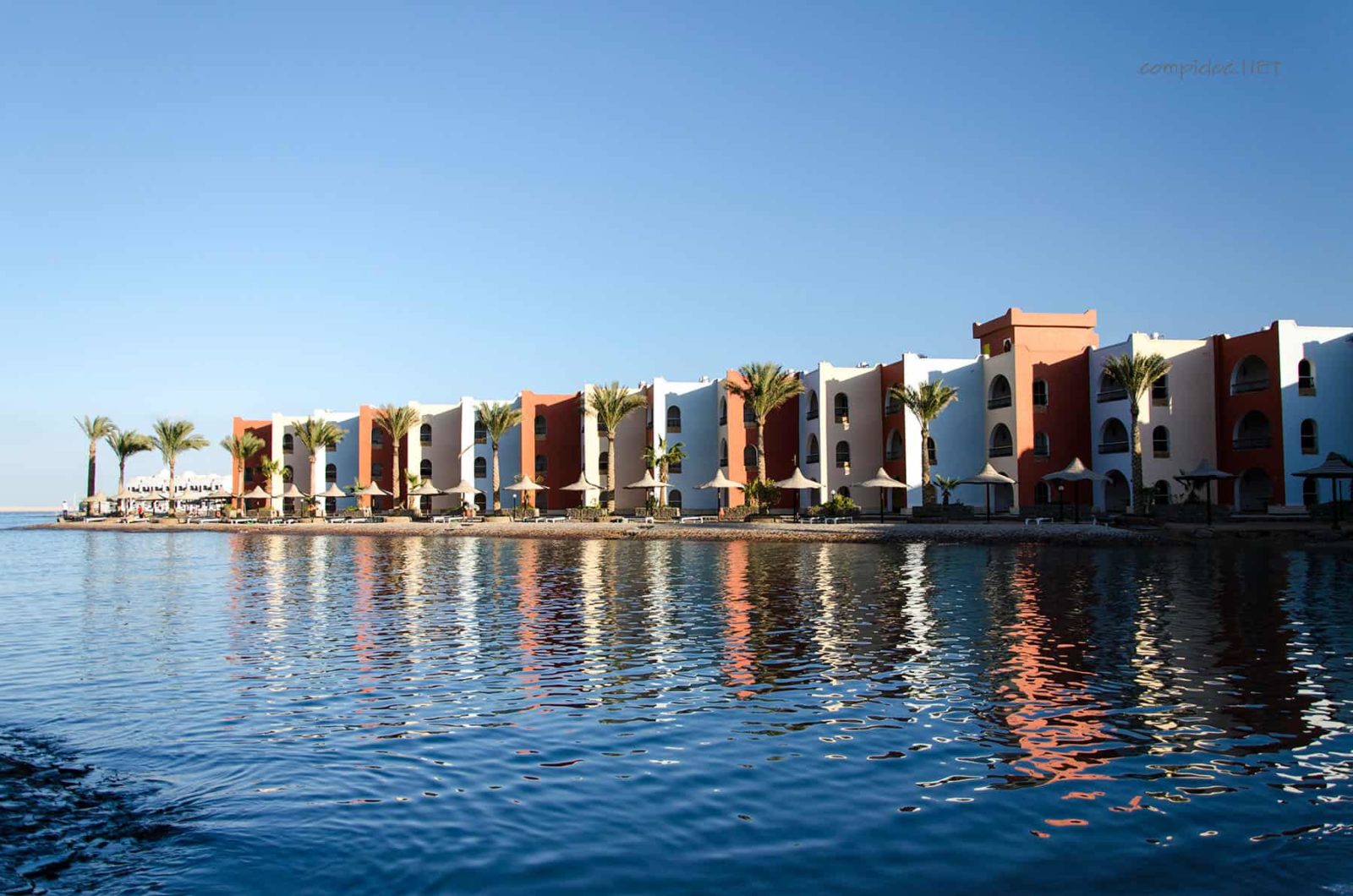 Colorful beachfront buildings in Hurghada reflected in calm water under a clear blue sky.
