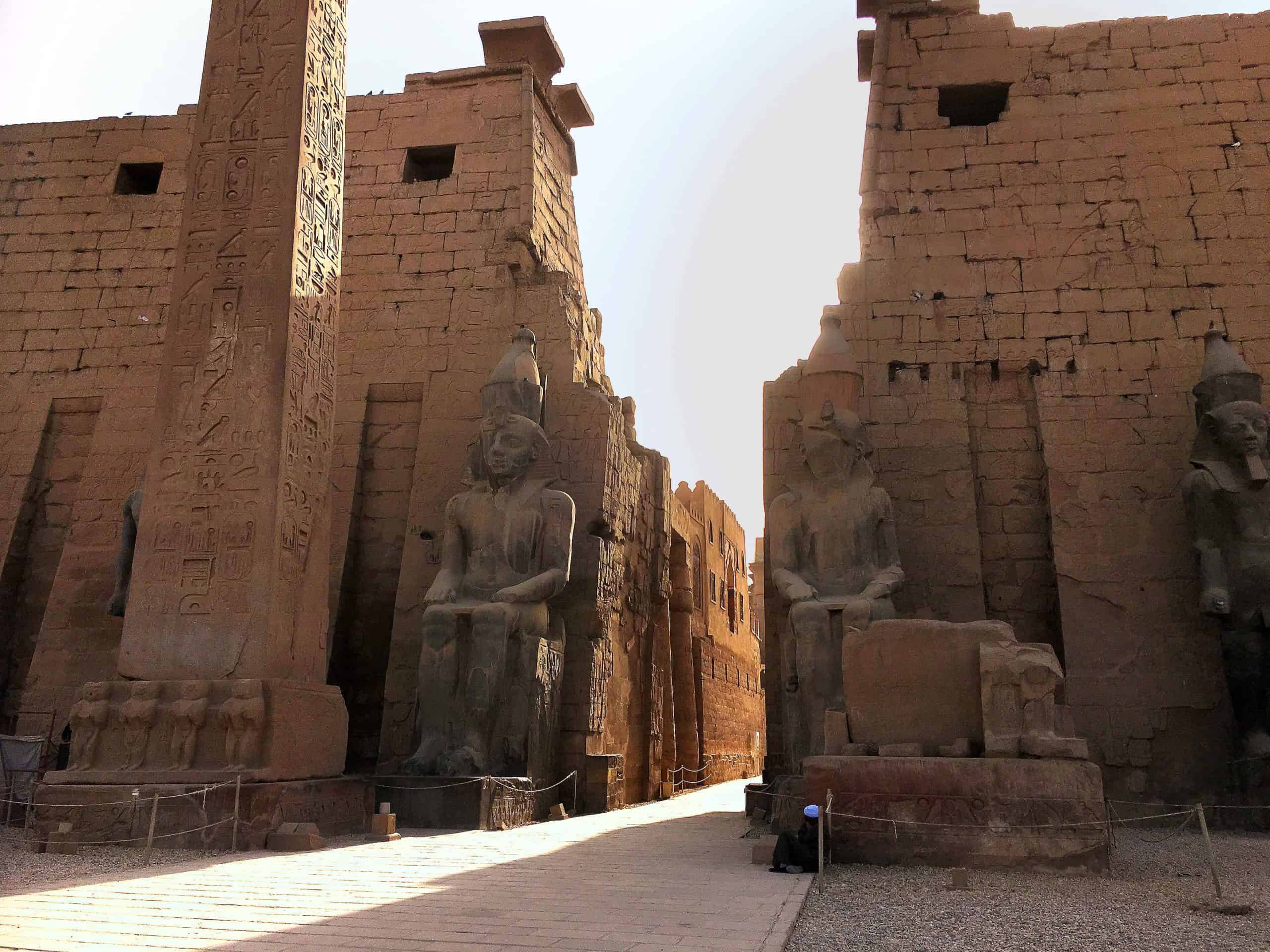 Luxors ancient stone statues and obelisk bask under the sunlight at a temple entrance.