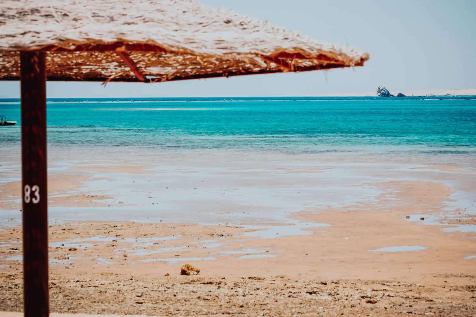 Relax at Sharm El Sheikh: a beach scene with a straw umbrella, sandy shore, and turquoise sea.