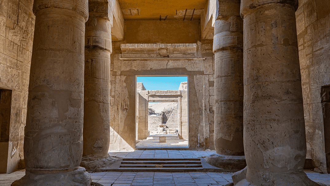 Interior of an ancient stone temple with large columns and an open doorway, echoing Egypts history.