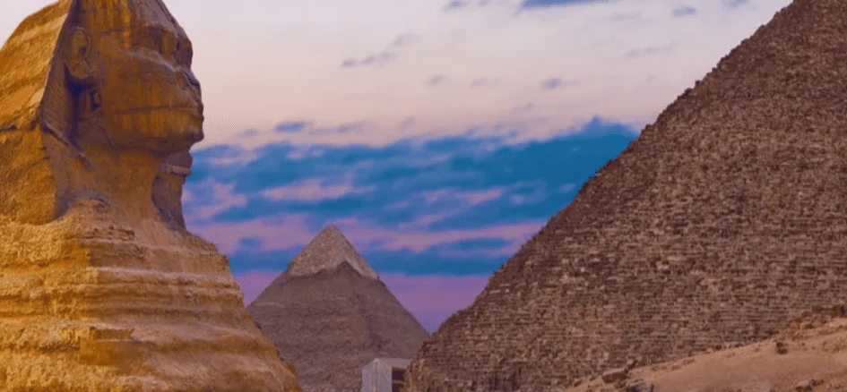 The Sphinx and Pyramids of Giza at sunset under a partly cloudy sky.