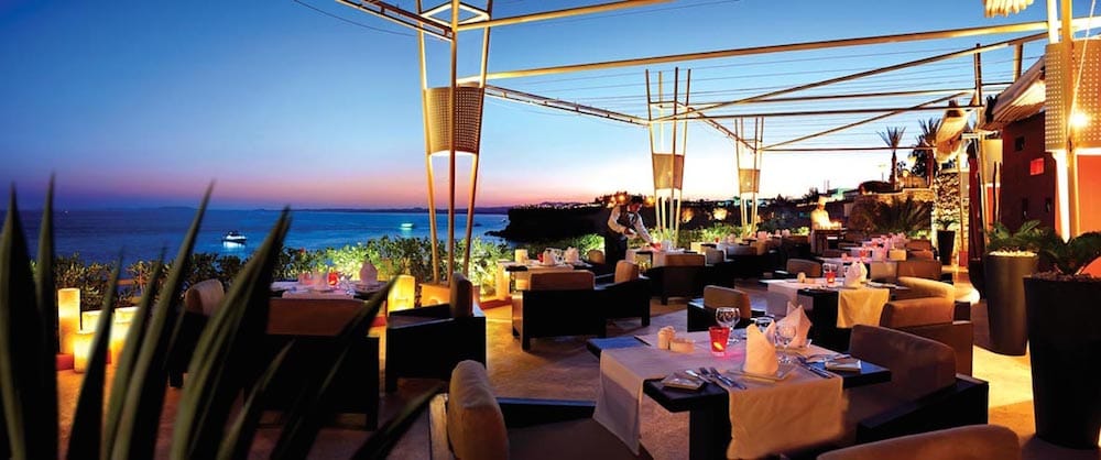Reef Oasis Beach Resorts outdoor dining offers ocean views at sunset with ambient lighting.