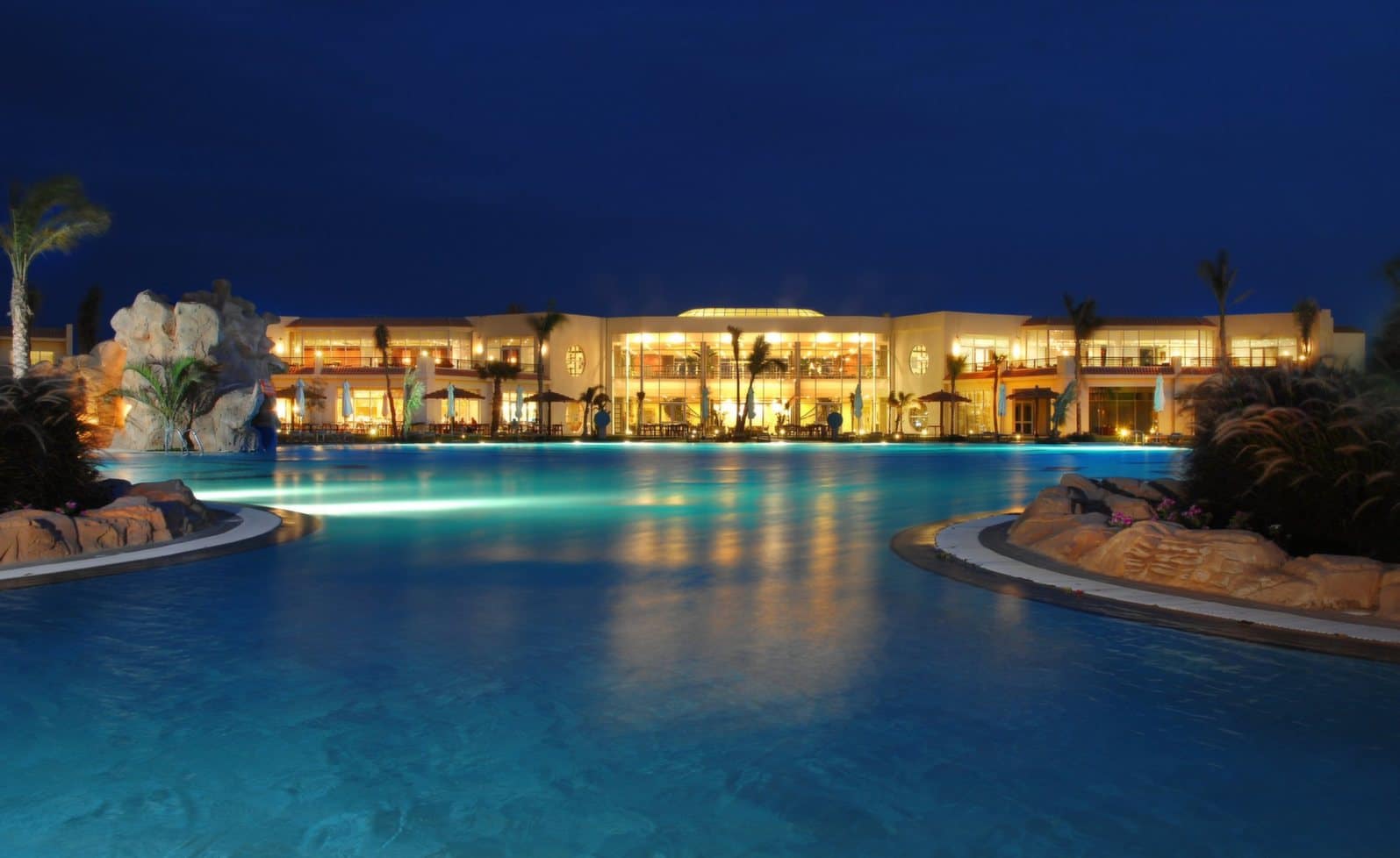 Hilton Sharks Bay luxury resort pool glows at night, framed by palm trees.