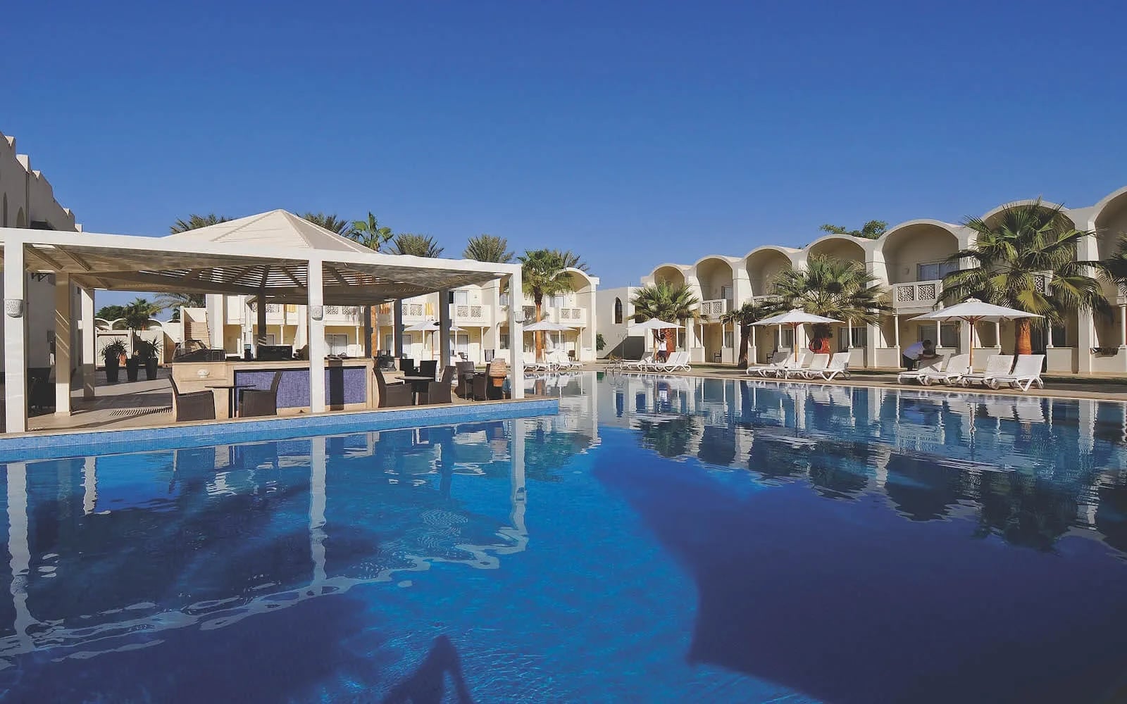 Reef Oasis Beach Resort: Pool with lounge chairs and cabanas under a clear blue sky.