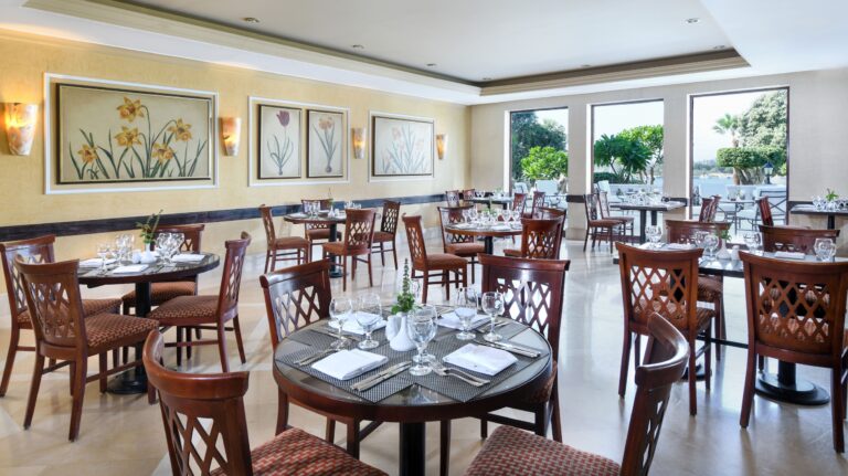 Empty restaurant at Iberotel Luxor Hotel with wooden tables, chairs, and floral artwork.