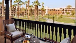 Balcony at Marriott Mena House: chairs, table, wine, fruit, and a lawn view with palm trees.