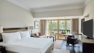 Marriott Mena House room with a large bed, seating area, TV, and balcony overlooking greenery.