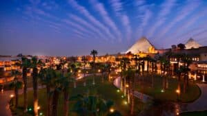 Night view of palm trees, Marriott Mena House, and a large pyramid under a vibrant sky.