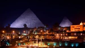 Night view of Marriott Mena House with illuminated pyramids and palm trees under a dark sky.