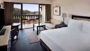 A Marriott Mena House room with a bed, sofa, and balcony overlooking a green landscape.