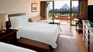 Marriott Mena House room with two beds, a sofa, and a balcony view of the distant pyramids.