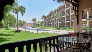 Balcony view of lush garden, pool, and Marriott Mena House with palm trees in the distance.