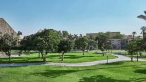 Lush green lawn with trees, a paved path, and Marriott Mena House near pyramids in the background.