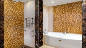 Bathroom at Sheraton Cairo with a glass shower, bathtub, and brown mosaic tiles.