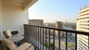Cityscape view from a Sheraton Cairo balcony with chairs, a table, and riverfront buildings.
