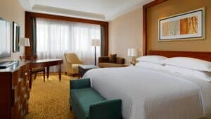 Sheraton Cairo room with king bed, desk, armchair, sofa, TV, and large curtained window.