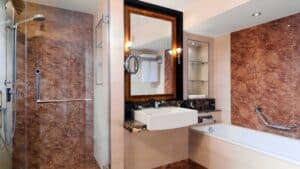 Modern bathroom at Sheraton Cairo, with a sink, mirror, shower, and brown marble walls.