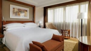 Modern Sheraton Cairo room with a large bed, armchair, and lamp near sheer-curtained window.