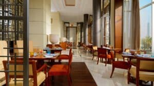 Modern restaurant interior with Sheraton charm, wooden chairs, dining tables, and large windows.