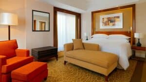 Room at Sheraton Cairo Hotel with a bed, armchair, bench, lamp, and artwork.