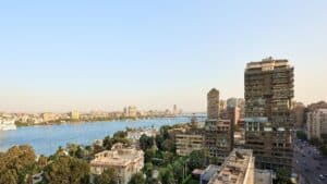 Aerial view of a riverside cityscape with tall buildings, trees, and Sheraton Cairo Hotel.