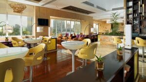 A modern lounge at Sheraton Cairo with yellow chairs, round tables, and city views.