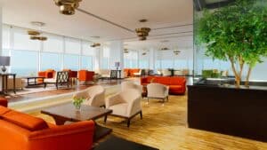 Modern lounge at Sheraton Cairo with orange seating, large windows, and a tall plant.