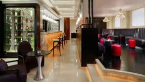 Modern bar lounge at Sheraton Cairo with stools, tables, and a lit wall display of bottles.