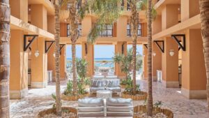 Courtyard at Sheraton Miramar with palm trees, cushioned seating, and ocean view through arches.