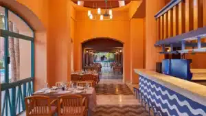 Sheraton Miramar vibes: orange walls, set tables, and a bar with blue wave pattern.