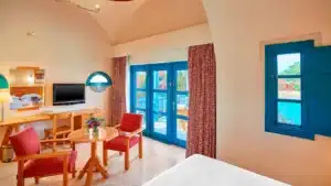 Sheraton Miramar Resort room: red chairs, wooden table, TV, blue-framed windows pool view.