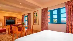 Sheraton Miramar Resort room with bed, seating area, TV, and large window with red curtains.