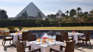 Outdoor dining at Marriott Mena House, with pyramids and a reflective pool amidst lush greenery.