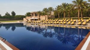 Outdoor pool at Marriott Mena House with yellow lounge chairs and palm trees reflecting on the water.