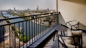 A balcony view at Sheraton Cairo Hotel & Casino overlooks the cityscape with a river and chairs.